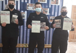 Trzech uczniów klas mundurowych stoi , trzymając w ręku dyplomy za udział w konkursie.