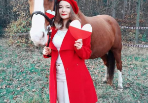 dziewczyna w czerwonym płąszczu i berecie w plenerze przy koniu, w ręku trzyma biało czerwone serce
